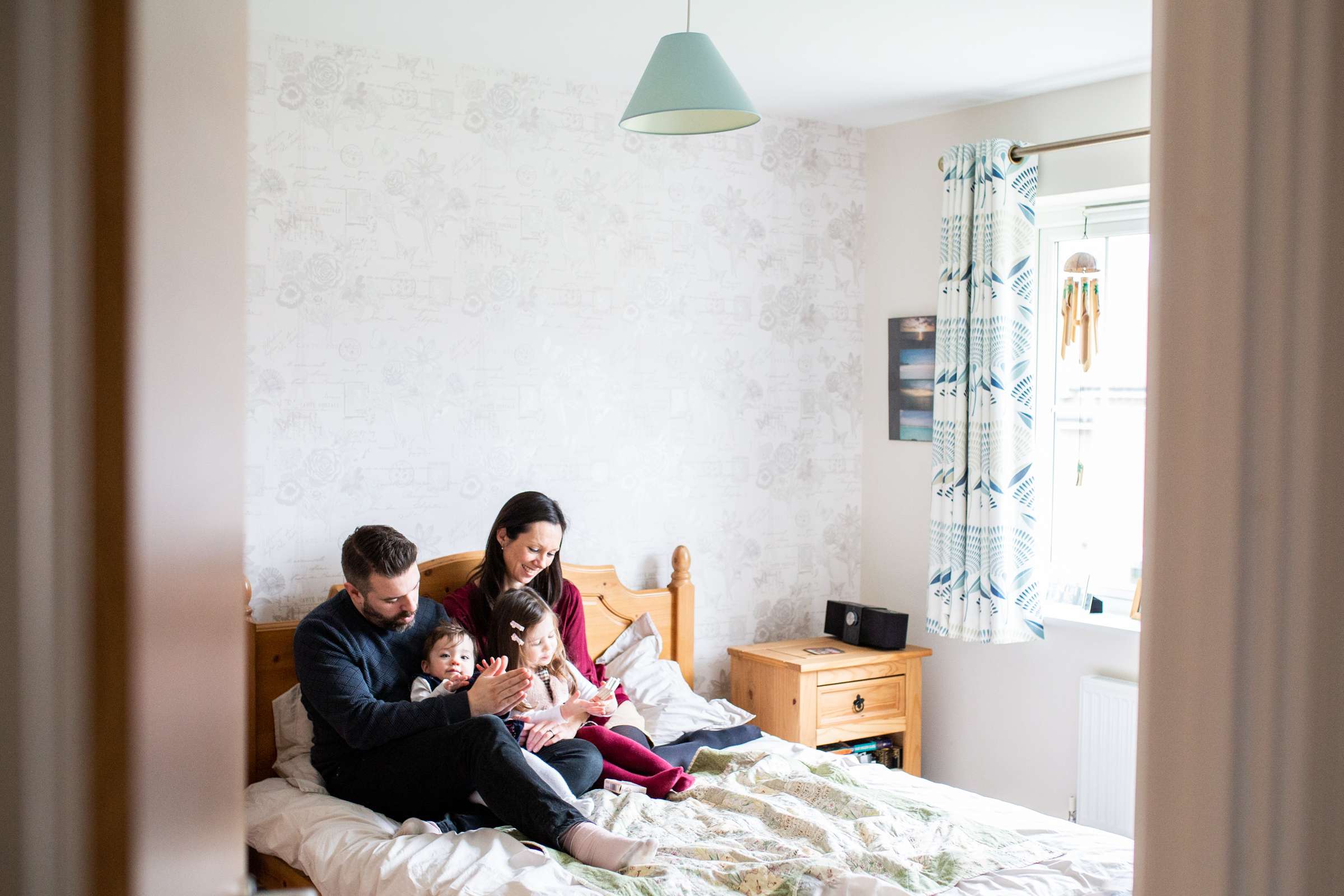 An indoor portrait photo of a family with two small children cuddling on the bed